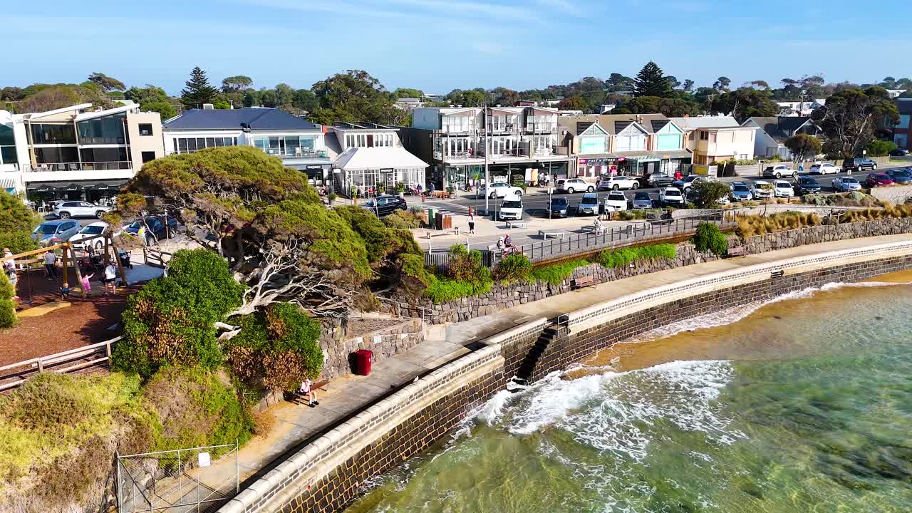 Aerial footage captures Point Lonsdale's coastline, showcasing vibrant greenery, coastal architecture, and gentle ocean waves under clear skies
