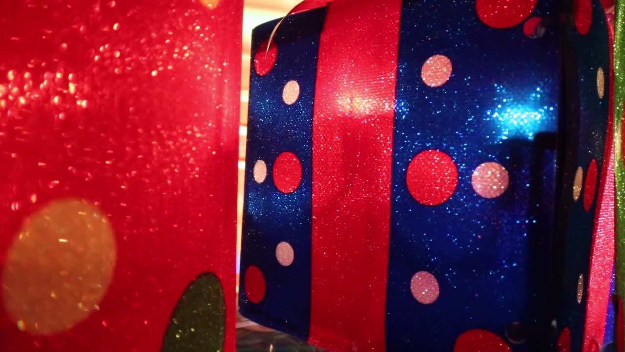 pasando por coloridos regalos de navidad iluminados, moviéndose hacia un regalo rojo - azul con lunares y un lazo rojo en la parte superior posicionado desplazado a la derecha