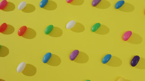 Video-of-overhead-view-of-rows-of-multi-coloured-sweets-over-yellow-background