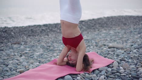 mujer haciendo yoga de pie en la cabeza en una playa