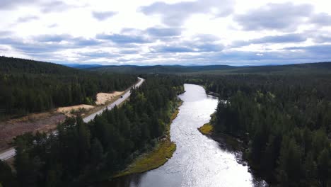 Car-on-a-highway-in-Lapland-alongside-lake-Inarinjarvi-carved-through-by-forest,-Inari,-Finland