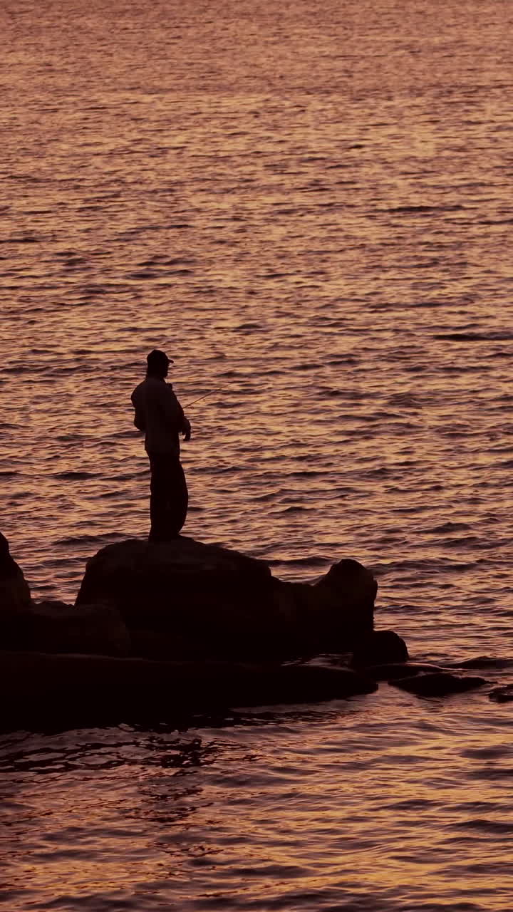 Fishermen on the rocks. Man's silhouette fishing at sunset. Freshwater fishing, catch of fish. Vertical video