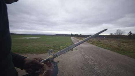 modern black swordsman warrior awaiting battle opponent in open field under grey sky, europe, 4k | muscular, intimidating, shadow, figure, blurry, dark clothes, powerful, close up, examine, artifact