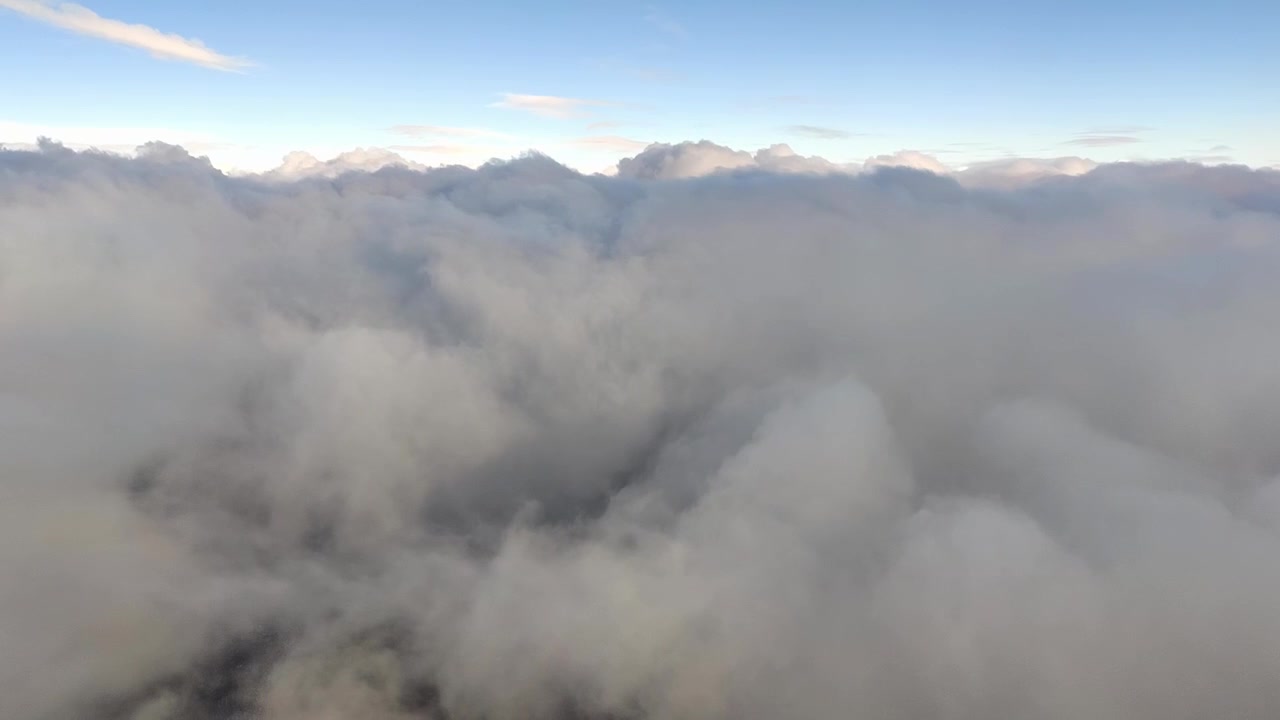 Thick dense clouds fill the lower frame, with blue sky and bright sun above. Viewed from airplane window during flight