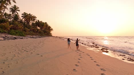 romantic aerial drone view of a couple enjoying the golden sunset on geiymiskih fannu beach in fuvahmulah, maldives.
