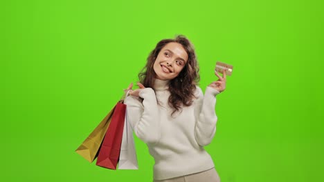 la mujer está mirando a la cámara y sonriendo. está sosteniendo bolsas de compras y agitando una tarjeta de crédito. está de pie sobre un fondo verde. pantalla verde. 4k