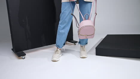 casual modern lifestyle look. girl in jeans and white sneakers holding a leather stylish rucksack. black screen at backdrop.