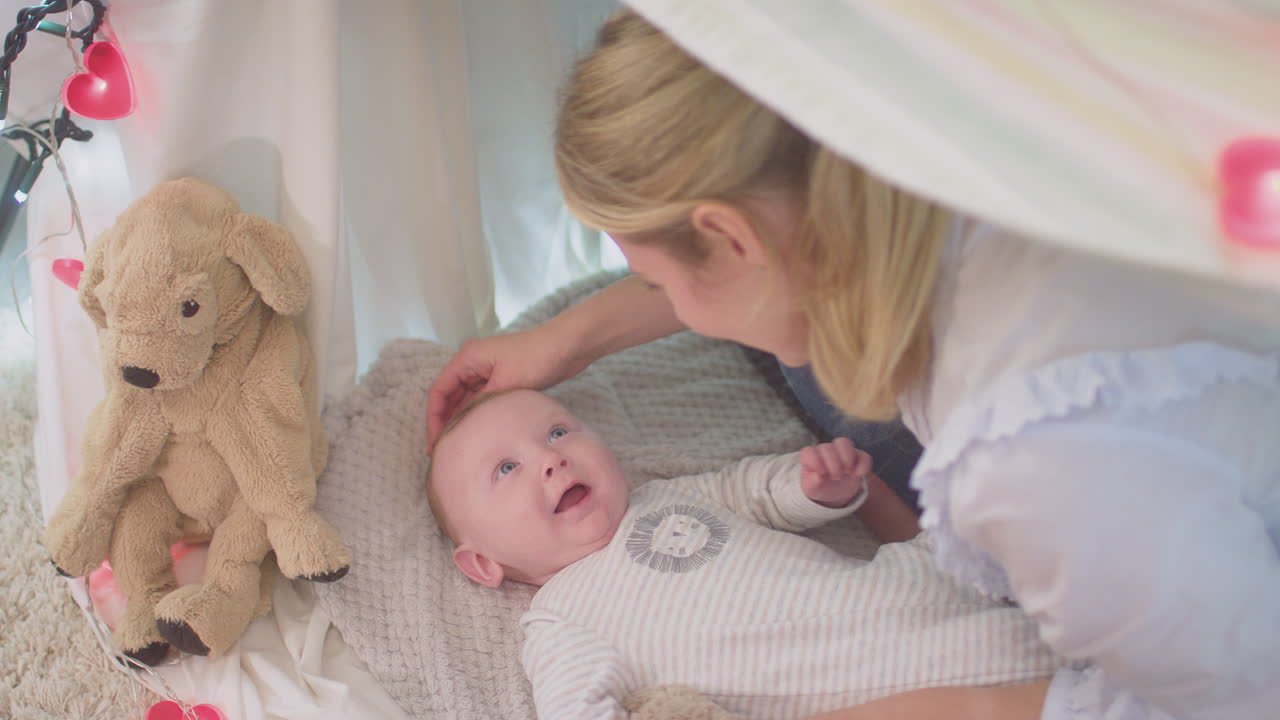 Loving mother cuddling baby son lying on rug in homemade camp in child's bedroom at home - shot in slow motion