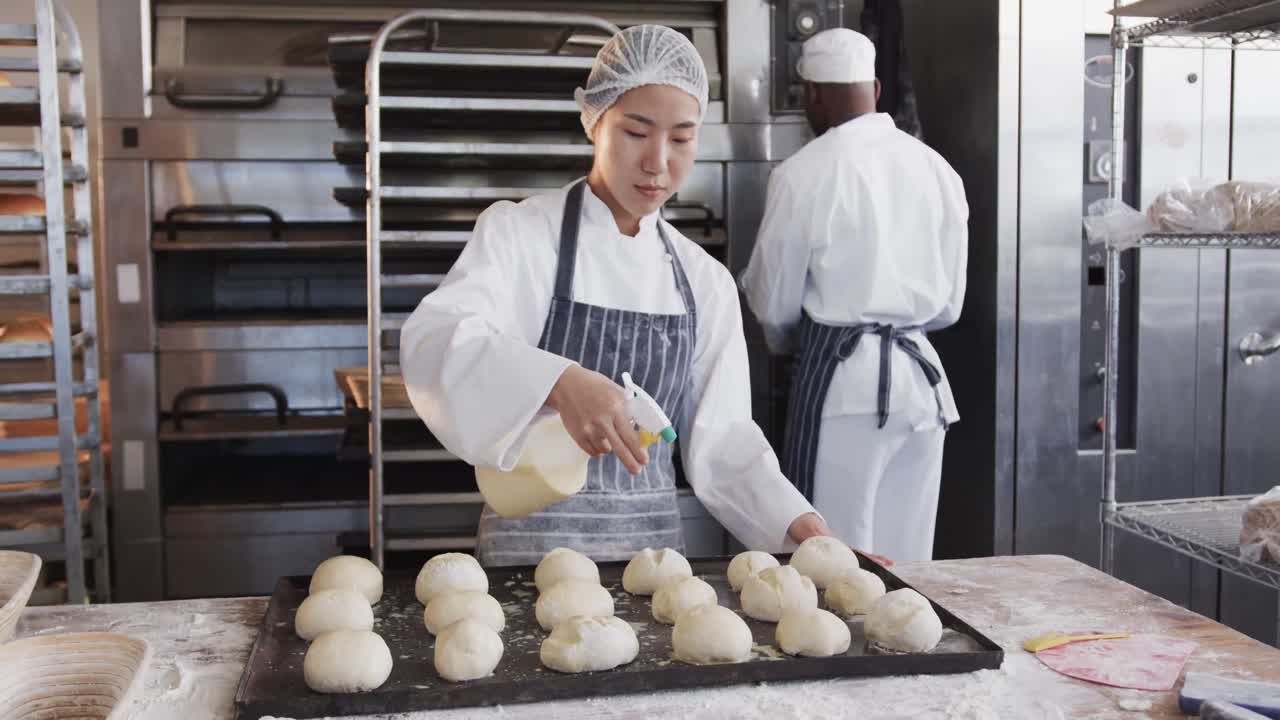 Diverse bakers working in bakery kitchen, spraying rolls in slow motion