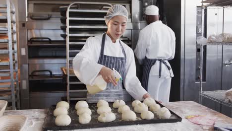diverse bakers working in bakery kitchen, spraying rolls in slow motion