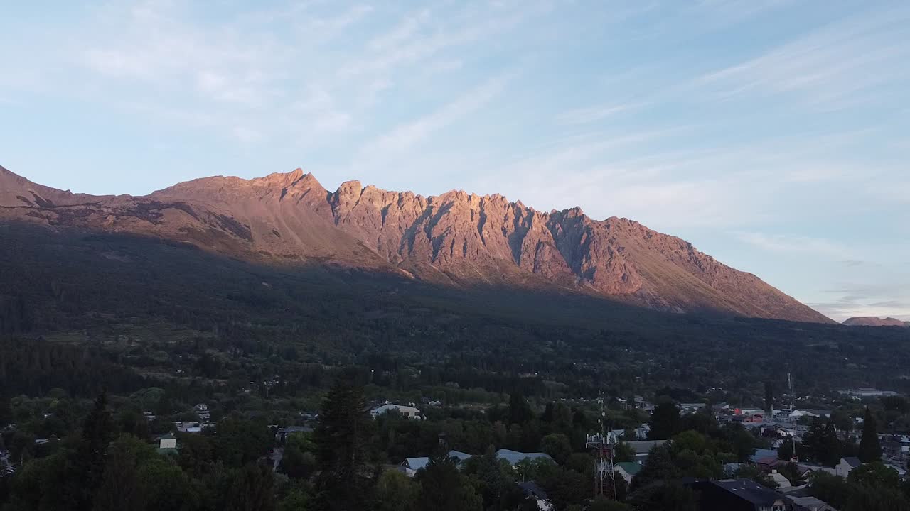 toma aérea de un pueblo y una alta montaña de piedra en el fondo, con el sol reflejándose en ella
