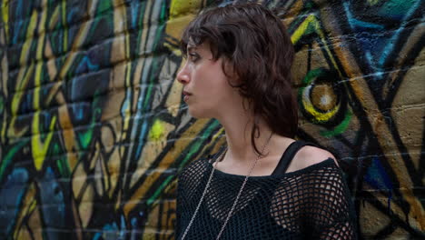 retrato de moda al aire libre de una mujer joven de estilo alternativo apoyándose en una pared cubierta de graffiti en la calle de la ciudad de londres, reino unido, en tiempo real.