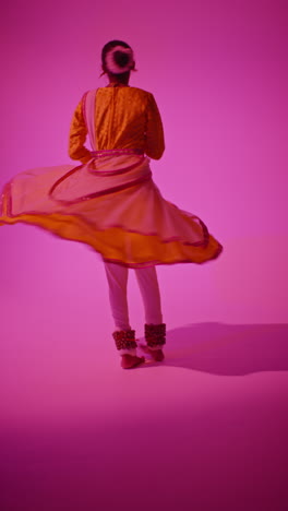 video vertical de una bailarina de kathak giratoria realizando un baile vestida con el vestido tradicional indio contra un fondo púrpura