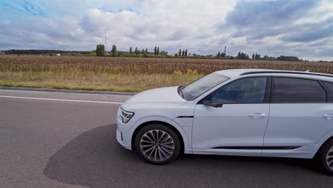 Aerial view on a light audi car on the road. White luxury car moving on highway on natural field background.