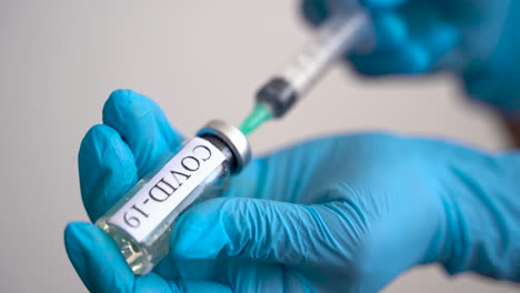 close up of hands with medical gloves filling a syringe with a vaccine for covid 19