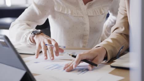 hands of diverse female colleagues in discussion using tablet in office, slow motion