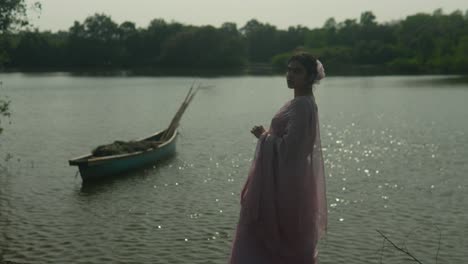 woman in vintage dress by a lake with a canoe, evoking a serene, reflective mood, with glistening water highlights