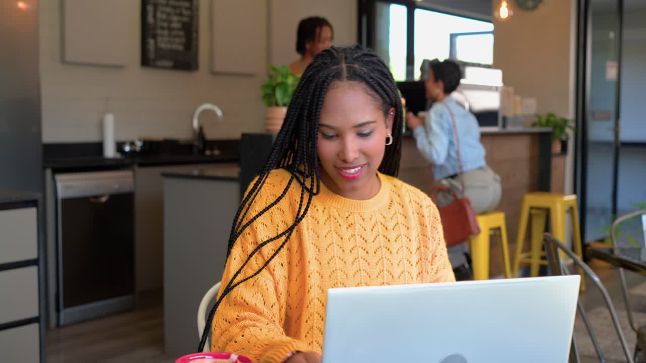 Glancing at smartphone, woman shifting and typing on laptop beside pink mug in cafe to focus