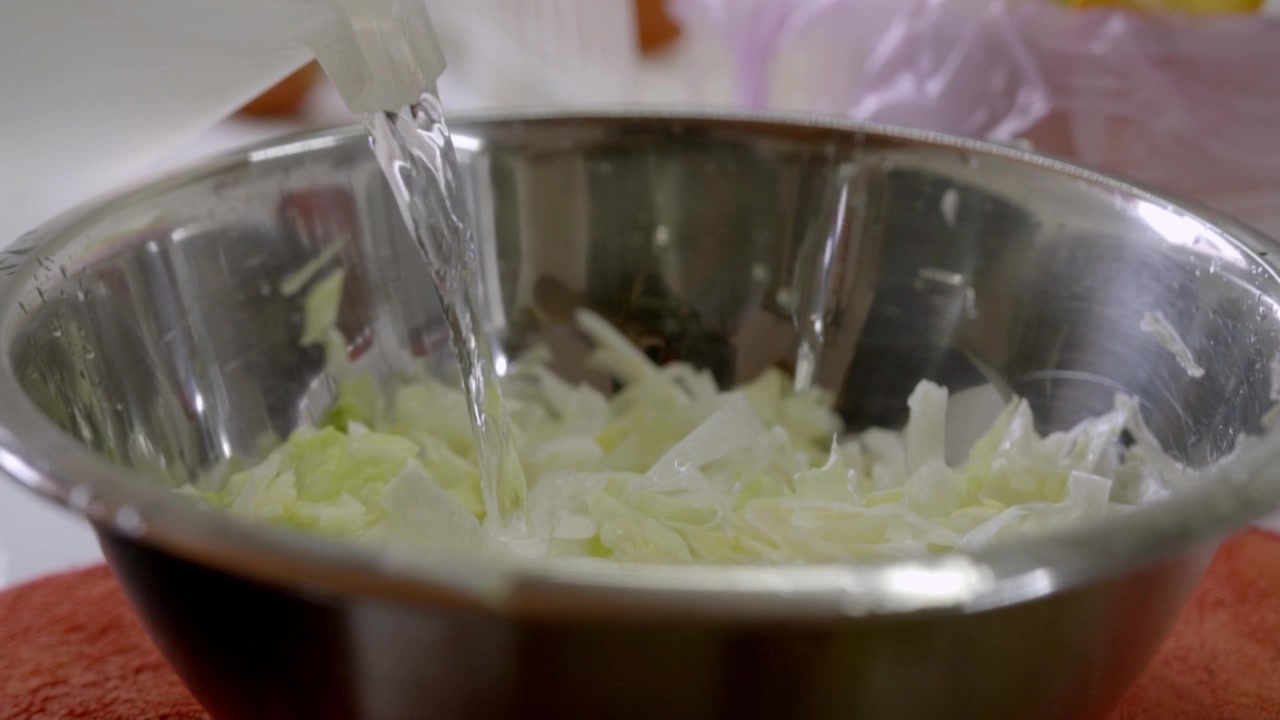 Water is being poured over shredded cabbage in stainless steel bowl during food preparation, helping clean fresh vegetables before making a salad or meal