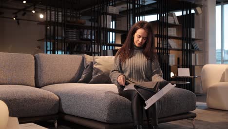 young woman sitting on couch choosing upholstery for lounge furniture in store young woman sitting on couch choosing upholstery for lounge furniture in store high quality footage