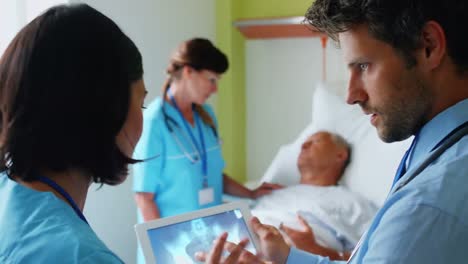médicos discutiendo rayos x en la tableta digital mientras la enfermera interactúa con el paciente en el fondo