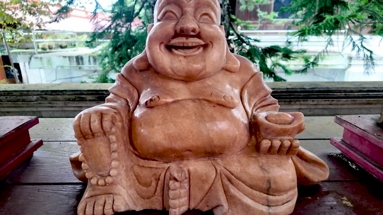 Wooden carving of a laughing Buddha, also known as Budai, sitting on a table