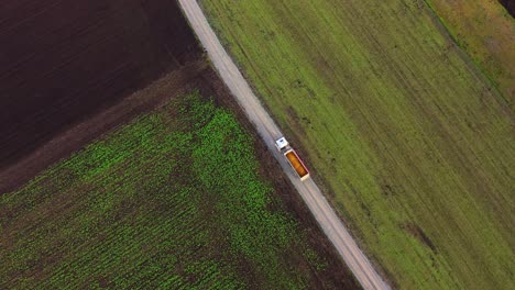 aerial view of loaded truck driving on country road through cultivated fields