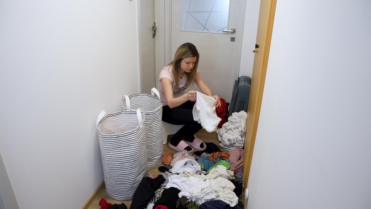 Donna che sistema una grande pila di biancheria sul pavimento di casa, faccende domestiche.
