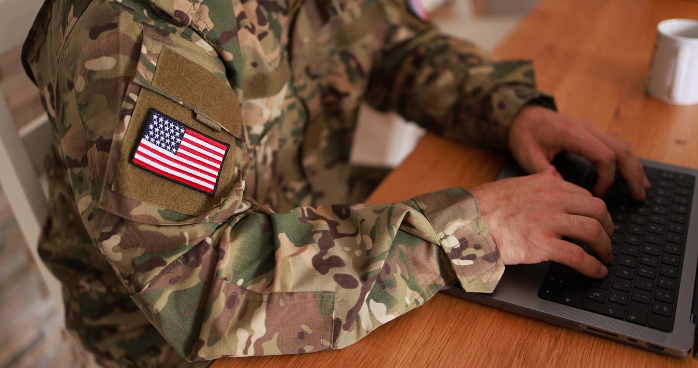 Soldato in uniforme mimetica che digita al laptop con una toppa della bandiera americana