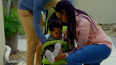 Front-view-of-young-black-parents-helping-to-sit-their-son-in-stroller-in-back-yard-of-their-home-4k