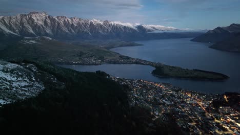 Increíble-Vista-Aérea-Nocturna-De-Queenstown-A-Orillas-Del-Lago-Y-La-Majestuosa-Cordillera