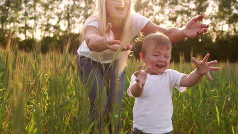 The-concept-of-a-happy-family.-In-the-rye-field-the-kid-walks-across-the-field-in-the-sun-setting-sun-looking-into-the-camera-Mom-stands-behind