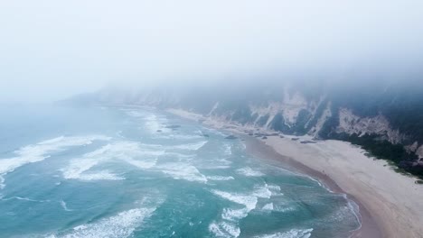 Eine-Luftdrohne,-Die-Unter-Einer-Wolkendecke-Fliegt,-Während-Ein-Tiefdrucksystem-Winterniederschläge-Und-Unruhige-Brandung-In-Sedgefield,-Westkap,-Südafrika,-Bringt