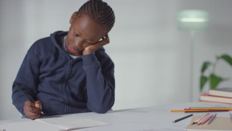 boy on asd spectrum at table at home concentrating on writing in school book