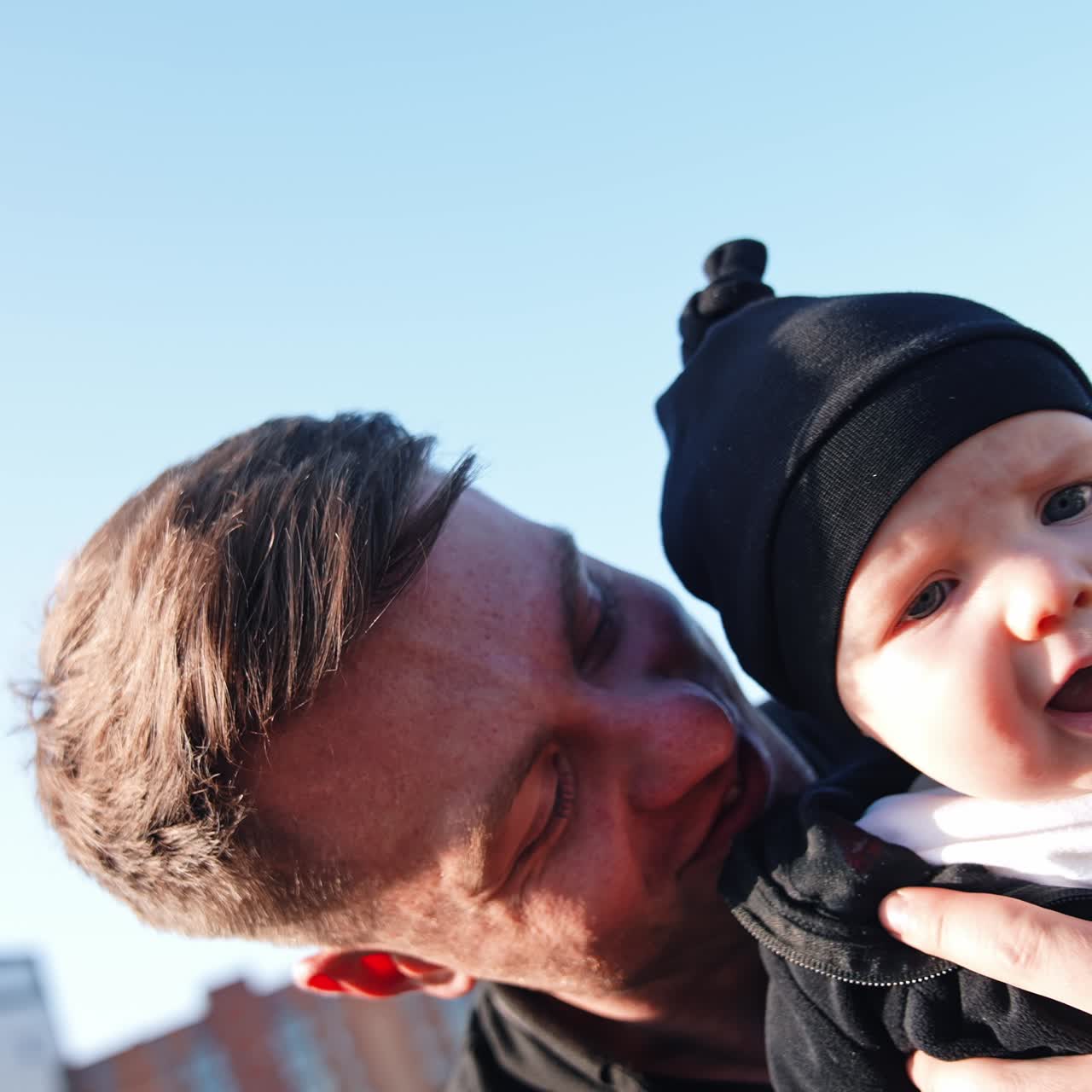 Face of Caucasian baby boy in a black cap. Smiling happy dad holding his child. Close up