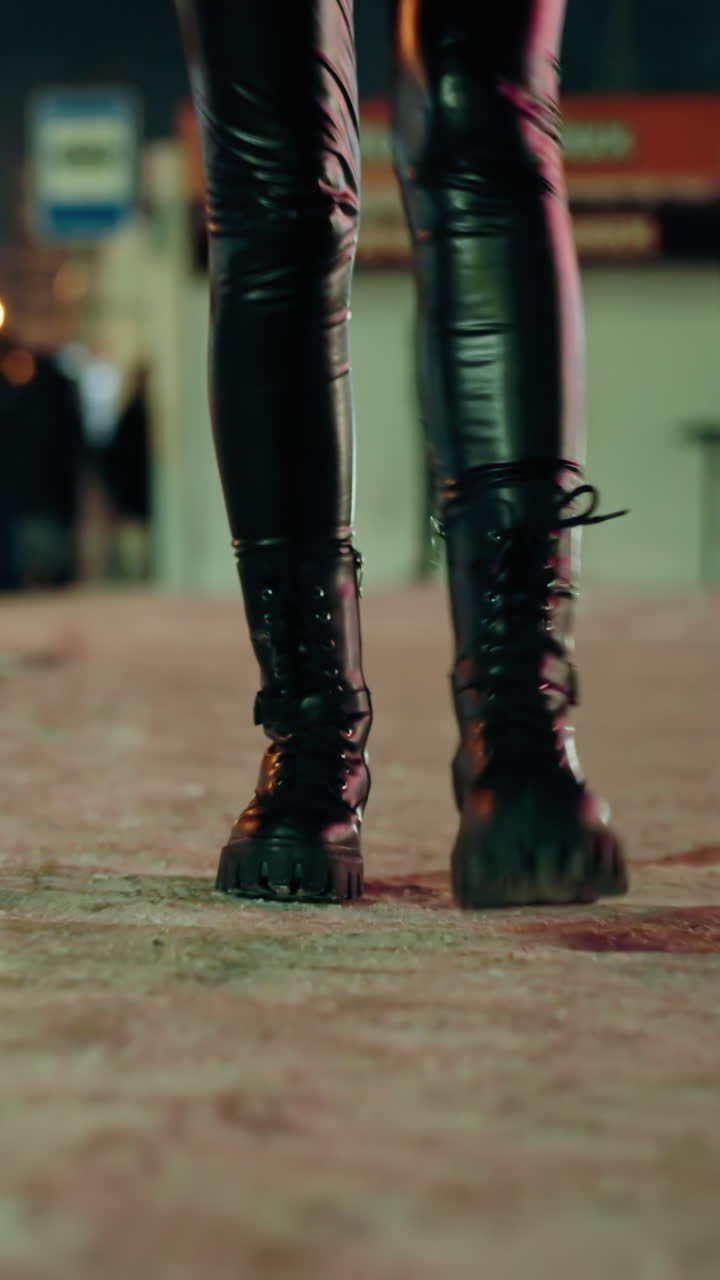 vista en primera persona de una mujer con pantalones de cuero negros y botas negras, caminando por la noche en una calle nevada, con luces borrosas de la ciudad