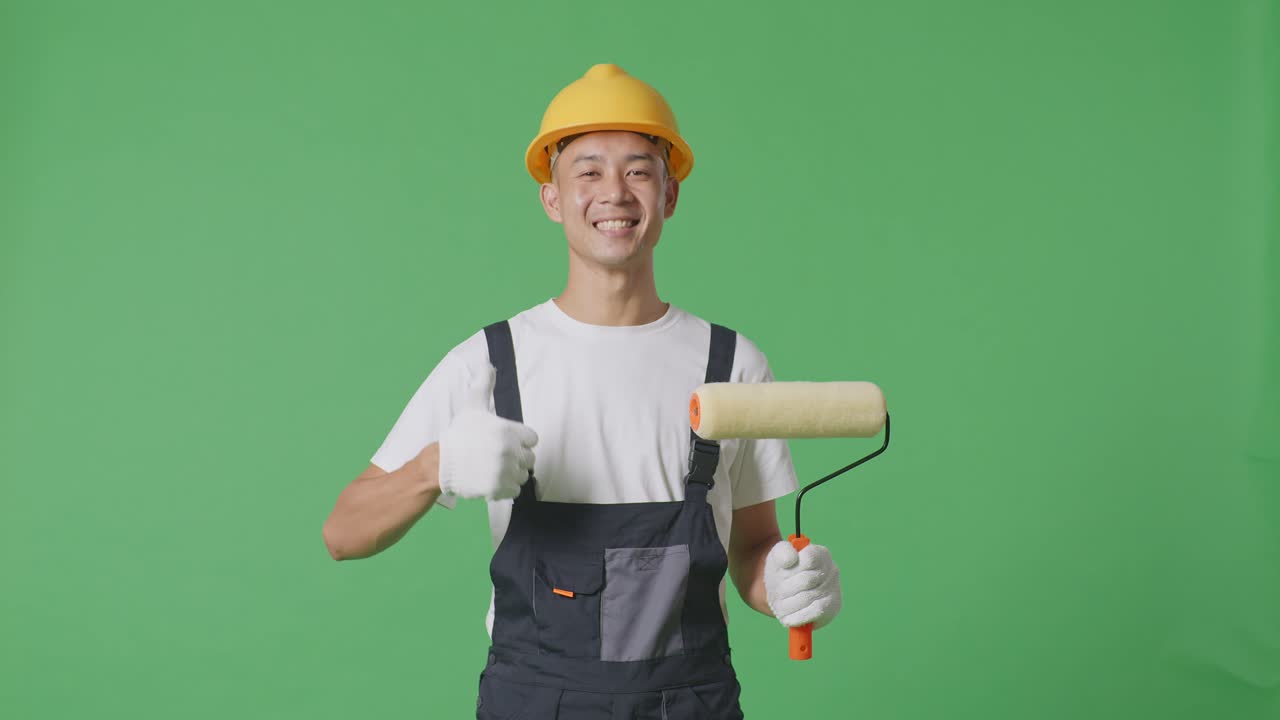 Asian Man Painter Wearing Safety Helmet Smiling And Showing Thumbs Up Gesture While Standing In The Green Screen Background Studio