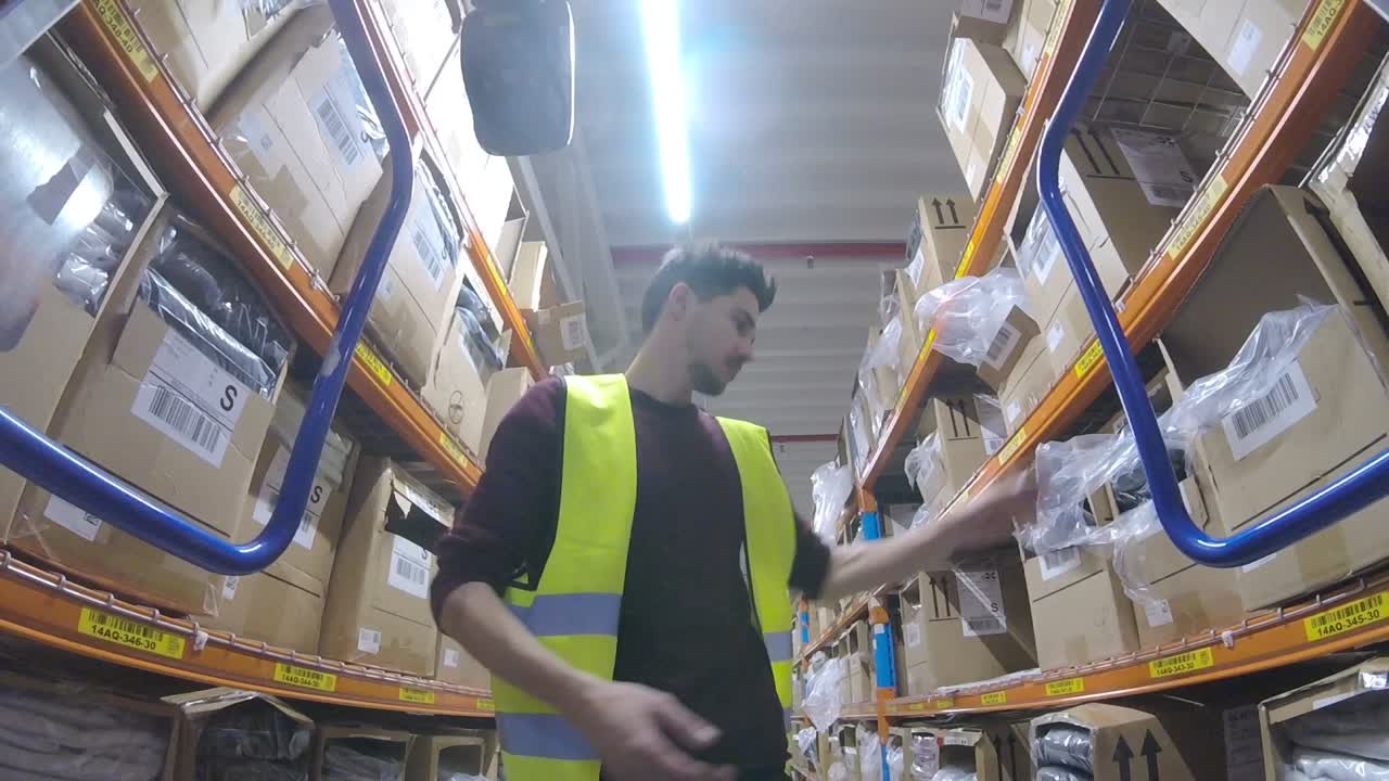 Wide angle shot of a male worker picking while pushing a trolley in a warehouse