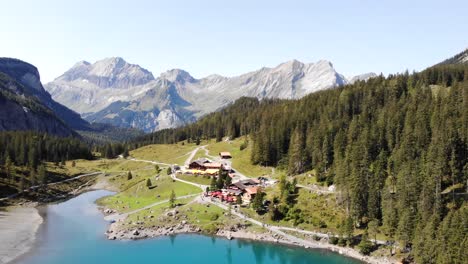 Aerial-flyover-over-lake-Oeschinensee-in-Kandersteg,-Switzerland-with-boats-on-the-turquoise-water-next-to-cliffs-on-a-sunny-summer-day