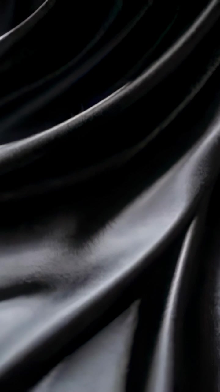 Vertical video: Starting camera pan across dark satin fabric on studio support to show sheen