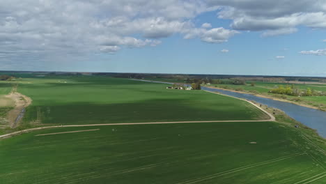 Aerial-flight-over-green-fields-beside-river-during-cloudy-and-sunny-day-in-rural-area