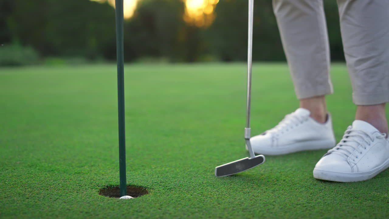 las piernas del jugador de golf se relajan en el agujero de la pelota de golf. el golfista posa en un campo verde y exuberante.