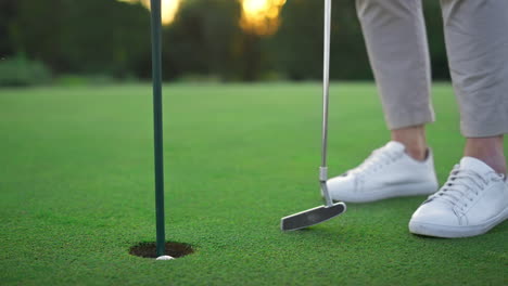 golf player legs relax at golfing ball hole. golfer posing on green lush course.