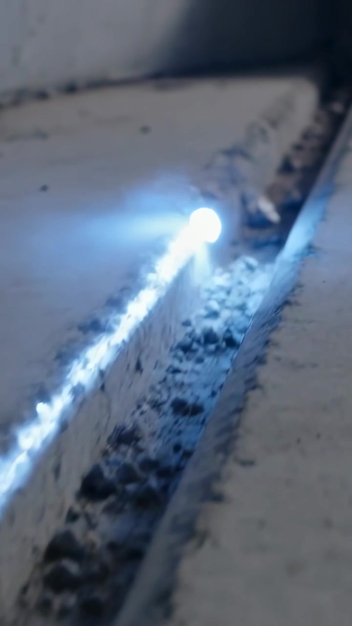 Video verticale: Appare alla fine una piccola luce blu che si muove lungo una scanalatura di cemento, rivelando ciottoli.