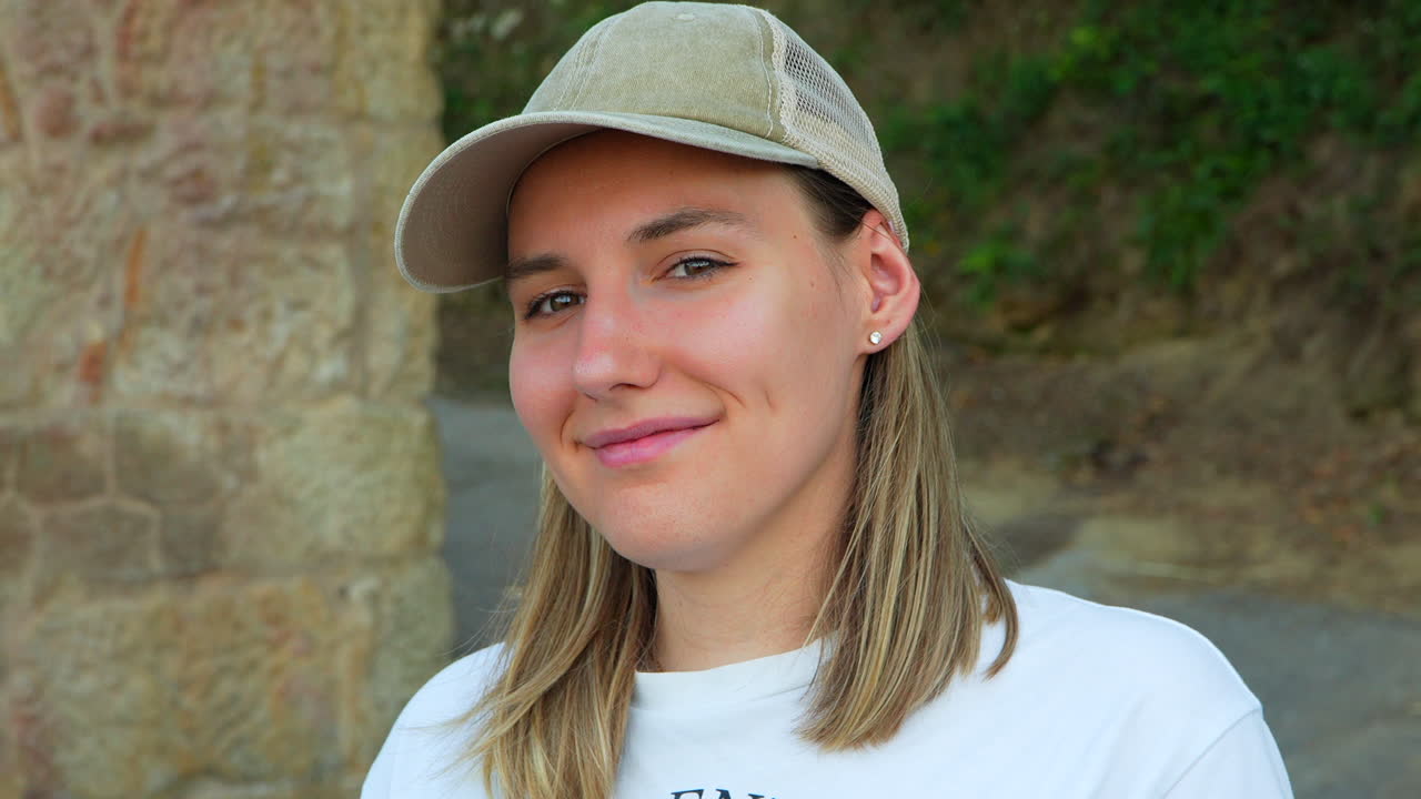 retrato de una joven rubia con gorra sonriendo tímidamente a la cámara