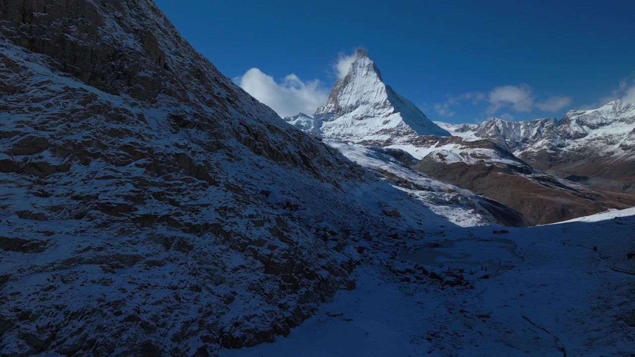 Cervino, famosa vetta montuosa, Lago Riffelsee, Zermatt, Alpi Svizzere. Drone aereo, prima neve fresca autunnale/invernale, cieli blu mattutini. Ferrovia del Gornergrat, sentieri escursionistici, Svizzera. Panoramica in avanti verso l'alto.