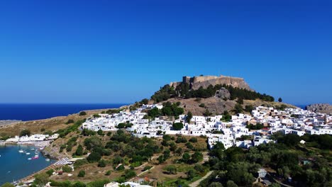 Pueblo-De-Lindos-En-Rodas,-Grecia-Con-La-Acrópolis-De-Lindos,-Casas-Y-El-Mar-Mediterráneo-Durante-El-Día-Filmado-Con-El-Dron