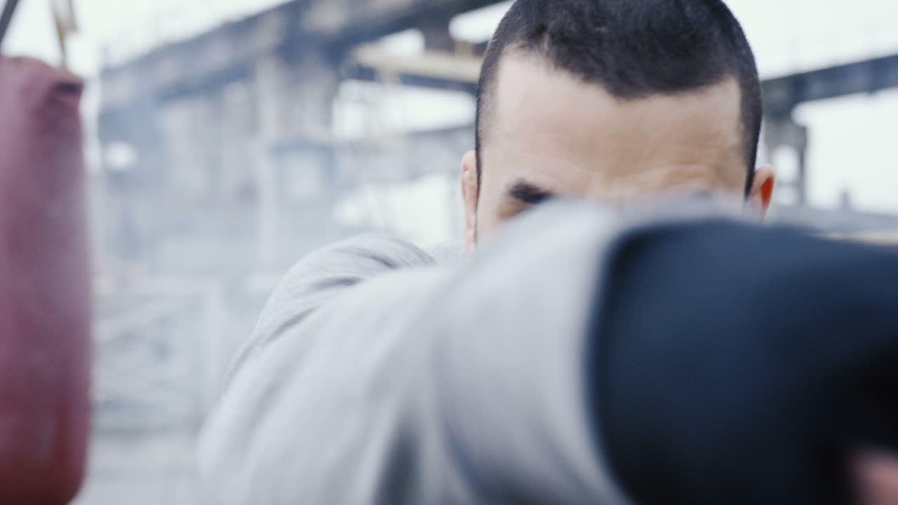 흐린 아침에 버려진 공장 밖에서 카메라를 향해 권투를 하는 잘생긴 수염 백인 남자의 클로즈업 보기