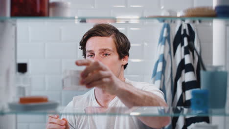 View-Through-Bathroom-Cabinet-Of-Man-Getting-Ready-For-Work-And-Moisturizing-Skin