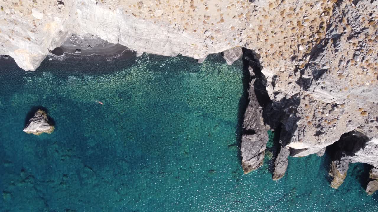 4k video drone top down view of a woman swimming in a breath taking turquoise beach under rocky cliffs during a sunny day